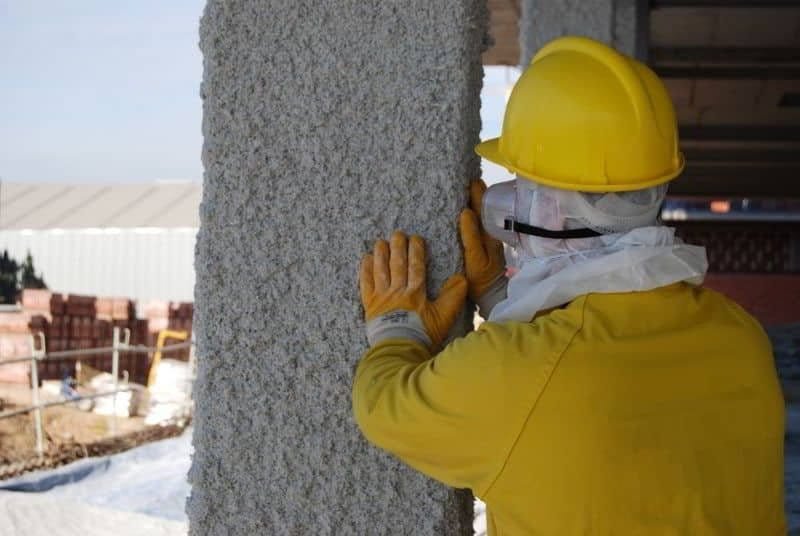 Técnico comprobando el espesor y la adherencia de la vermiculita proyectada sobre un pilar